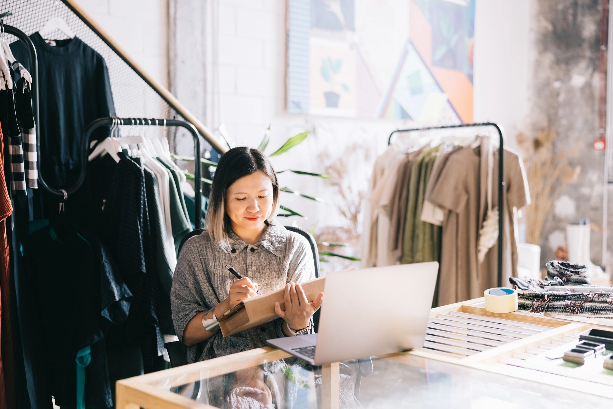 Shop owner packing an order while working on a laptop